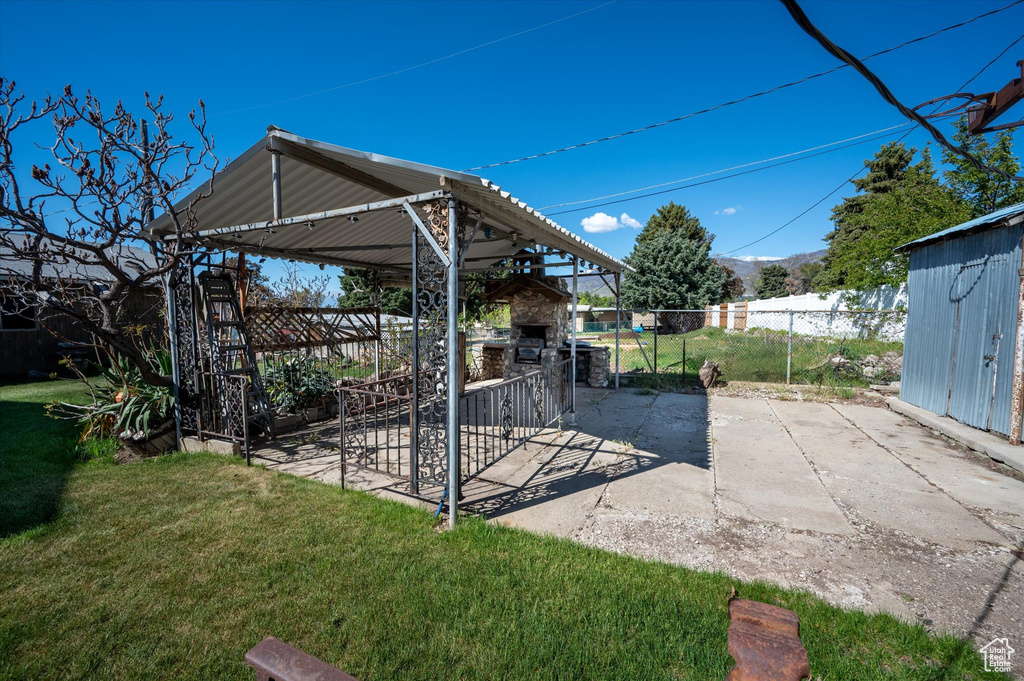 View of patio featuring fence, a shed, an outbuilding, and an outdoor stone fireplace
