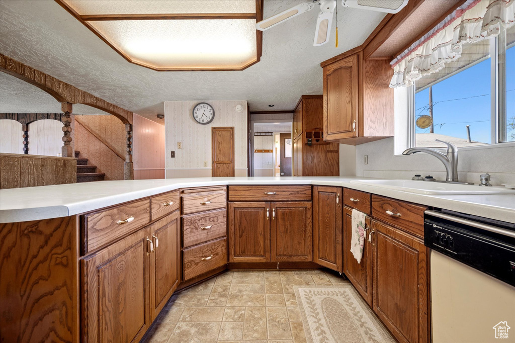 Kitchen with white dishwasher, light countertops, brown cabinets, and a sink