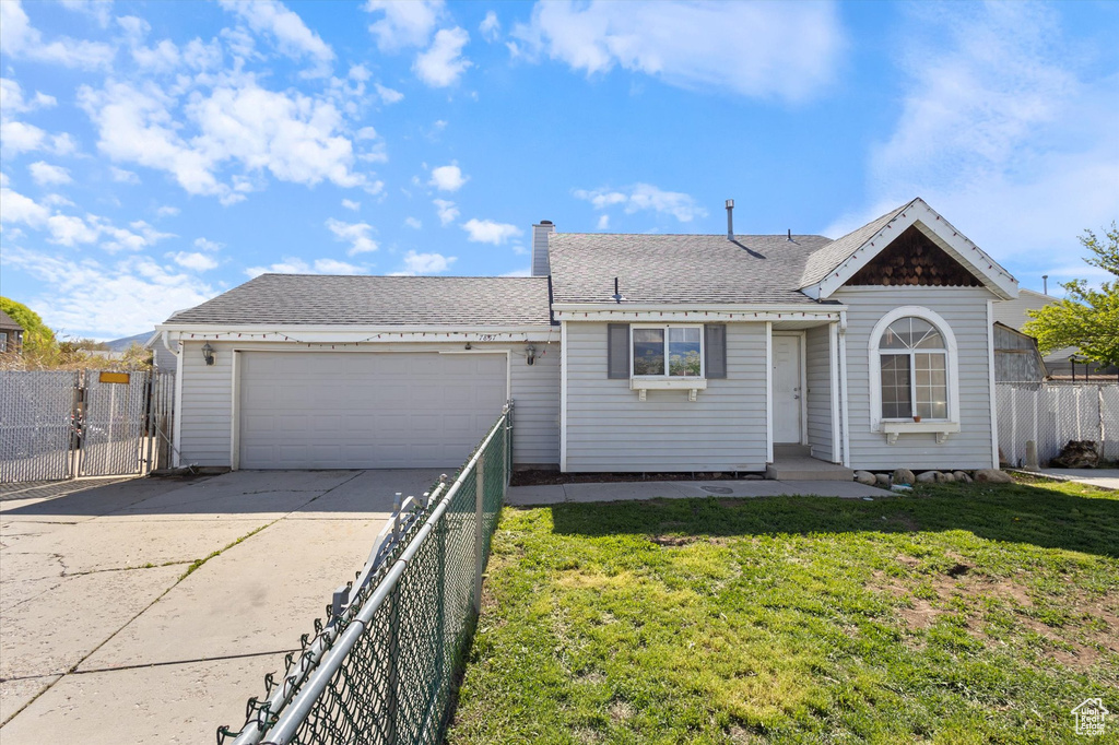 View of front facade featuring concrete driveway, an attached garage, fence, and a front lawn