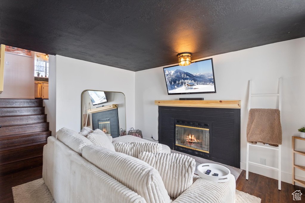 Living area featuring a glass covered fireplace, stairs, and wood finished floors