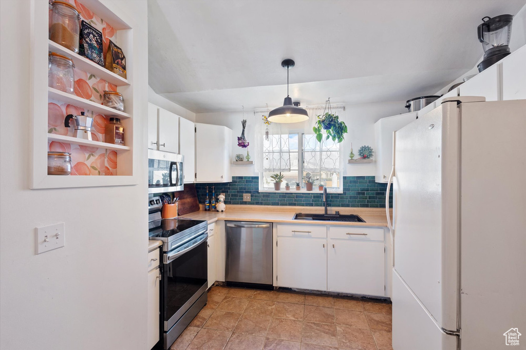 Kitchen with open shelves, appliances with stainless steel finishes, a sink, light countertops, and decorative backsplash