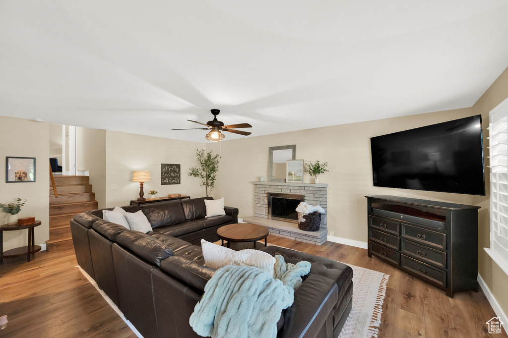 Living area with a ceiling fan, a stone fireplace, wood finished floors, and baseboards