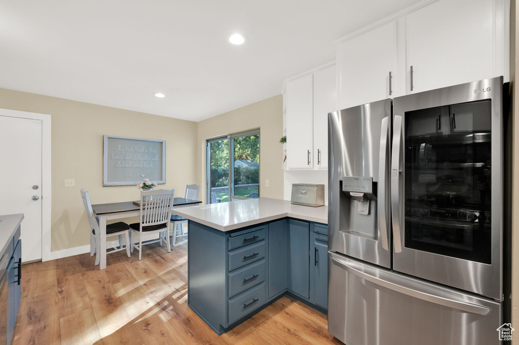 Kitchen featuring light wood-type flooring, white cabinetry, a peninsula, light countertops, and stainless steel fridge with ice dispenser