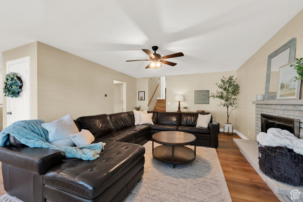 Living area with ceiling fan, a fireplace with raised hearth, baseboards, wood finished floors, and stairs