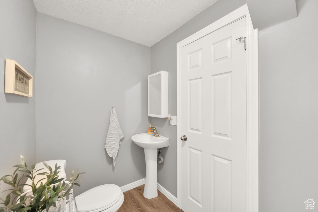 Half bathroom with toilet, wood finished floors, and baseboards