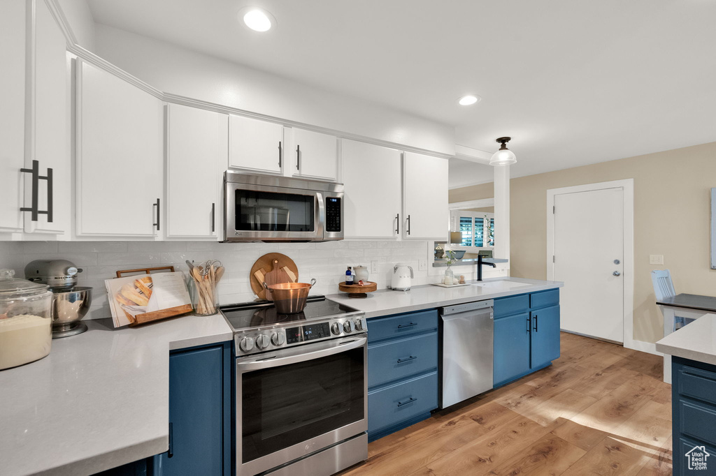 Kitchen featuring tasteful backsplash, blue cabinets, stainless steel appliances, white cabinets, and a sink