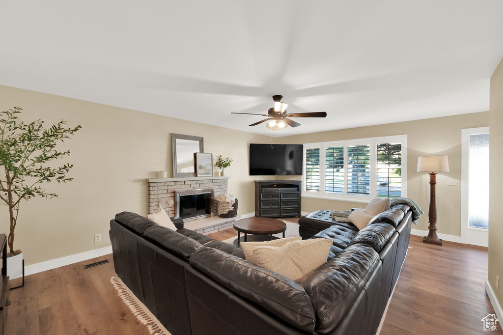 Living room with baseboards, visible vents, wood finished floors, and a stone fireplace