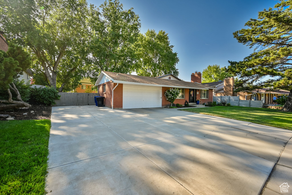 Ranch-style house with a front lawn, a garage, brick siding, driveway, and a chimney