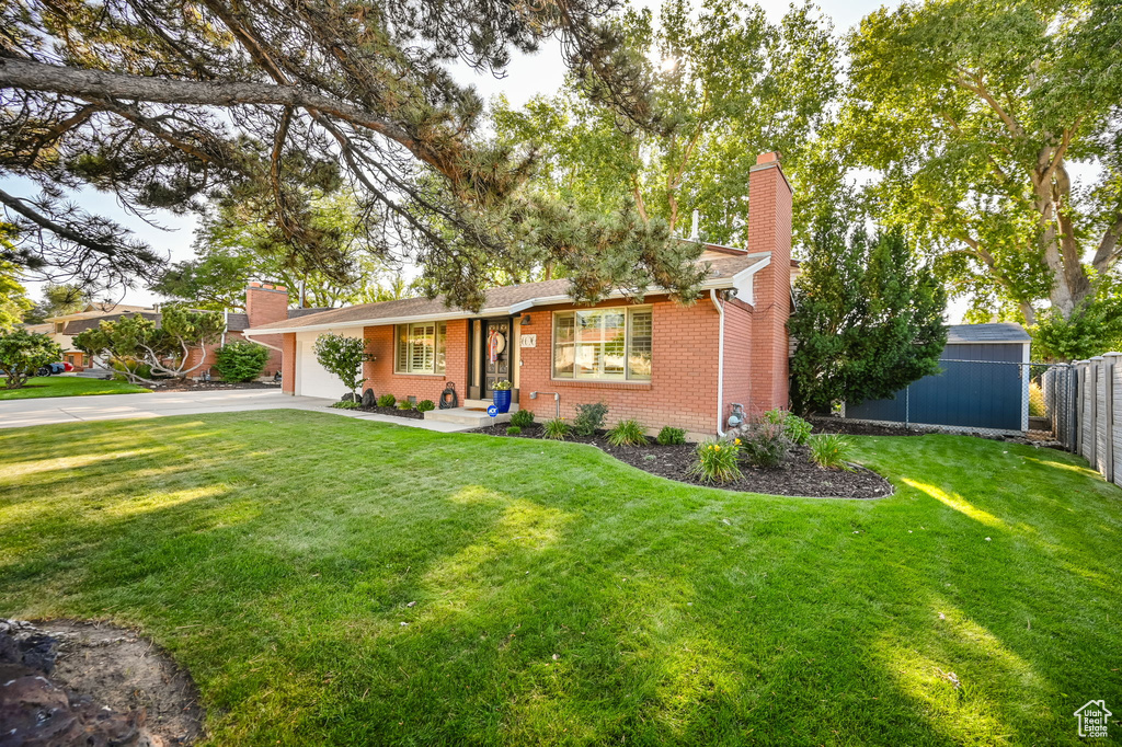 Ranch-style house featuring a front lawn, a chimney, aphalt driveway, brick siding, and fence