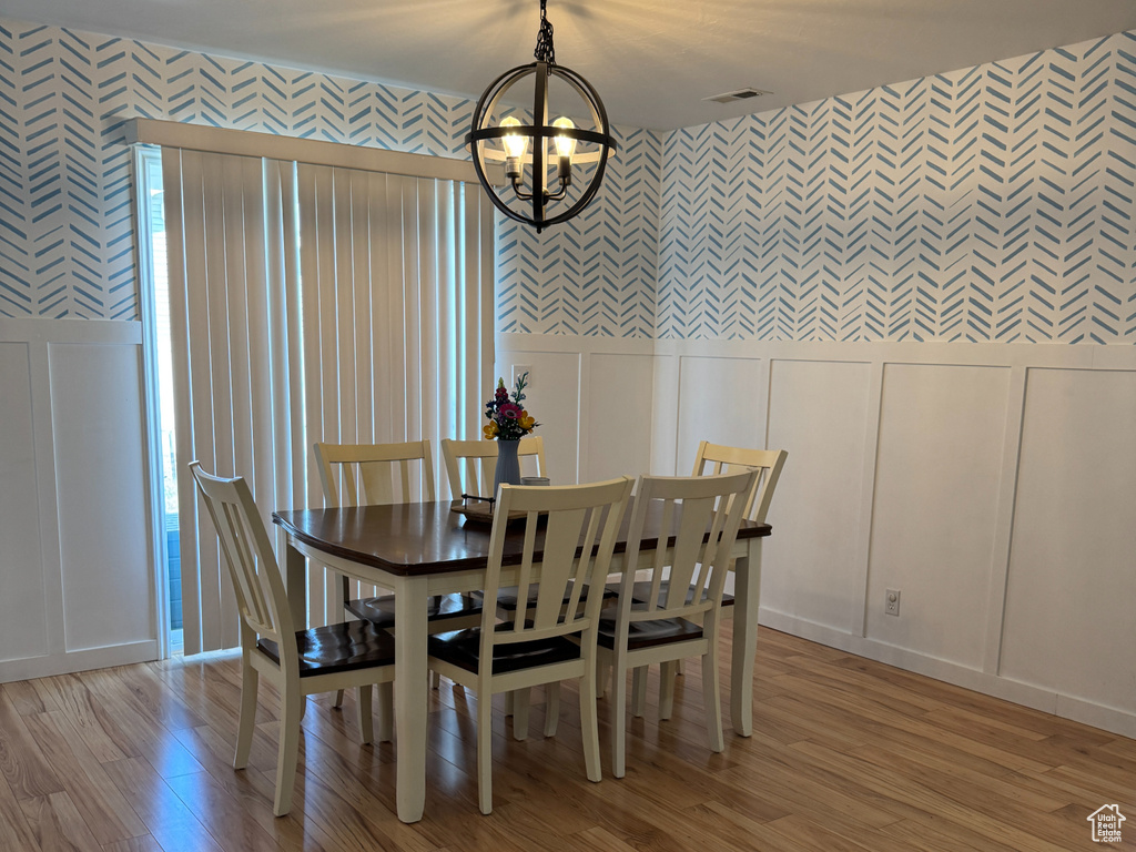 Dining room featuring light wood-style floors, a decorative wall, wallpapered walls, and a chandelier