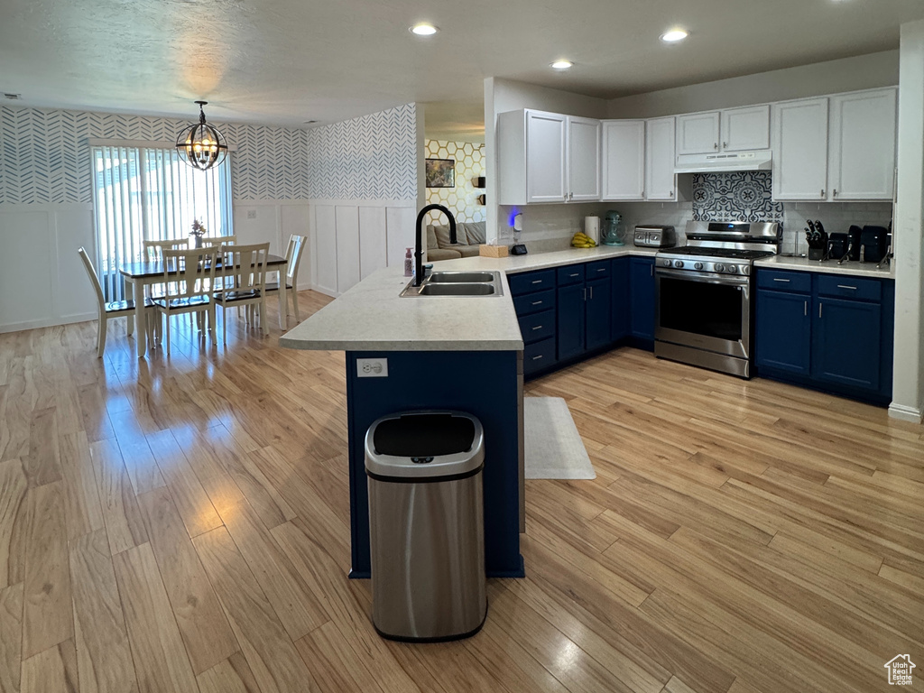 Kitchen featuring blue cabinetry, a sink, stainless steel range, light wood finished floors, and a peninsula
