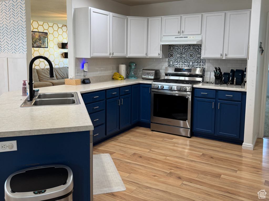 Kitchen featuring a sink, under cabinet range hood, stainless steel gas range oven, and blue cabinetry