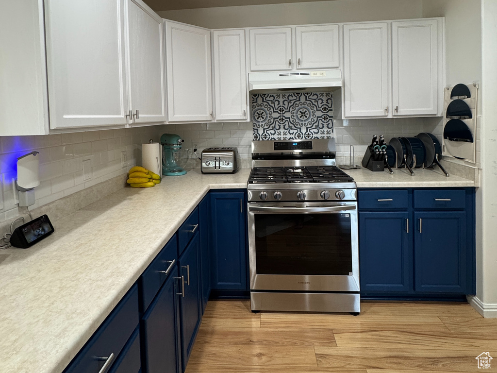 Kitchen featuring under cabinet range hood, stainless steel gas stove, white cabinets, and blue cabinetry