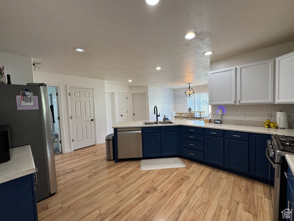 Kitchen with a peninsula, light wood-type flooring, a sink, appliances with stainless steel finishes, and blue cabinetry