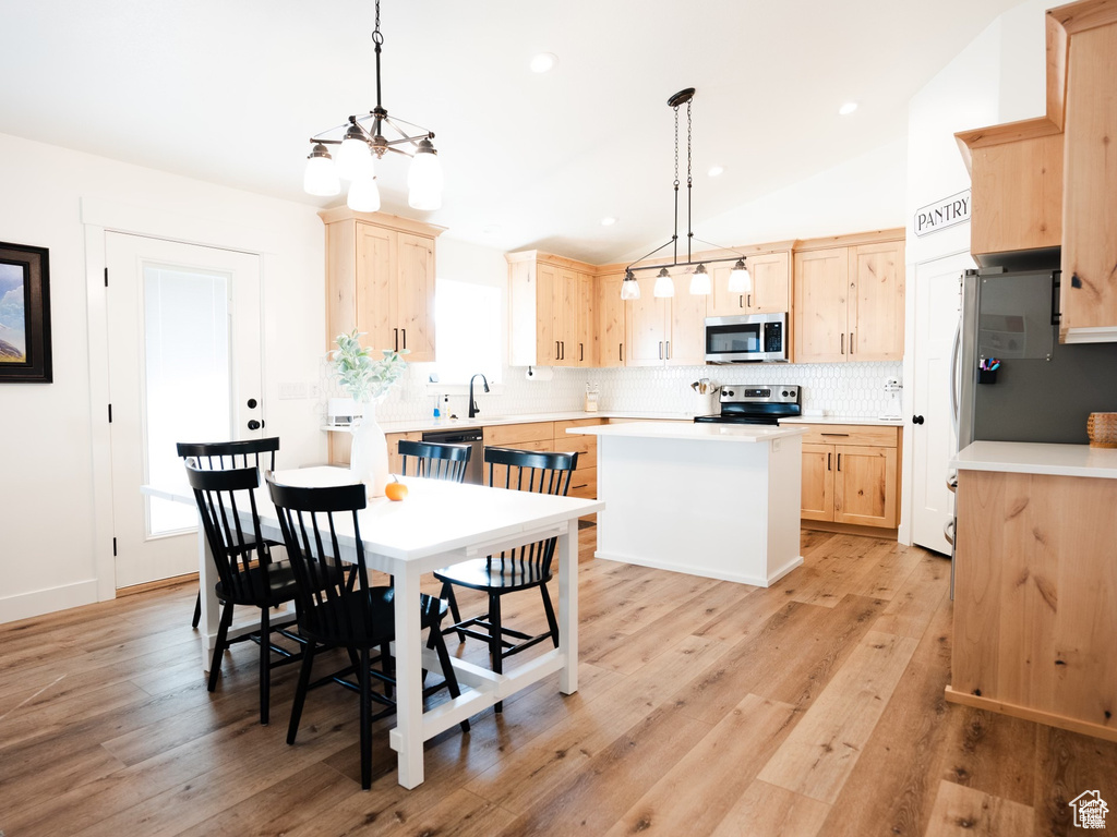 Kitchen featuring appliances with stainless steel finishes, light brown cabinets, light countertops, backsplash, and a kitchen island