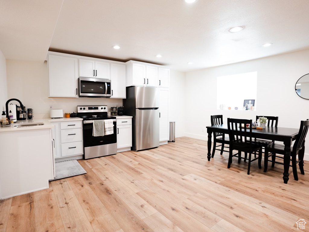 Kitchen with a sink, stainless steel appliances, recessed lighting, white cabinetry, and light wood-type flooring