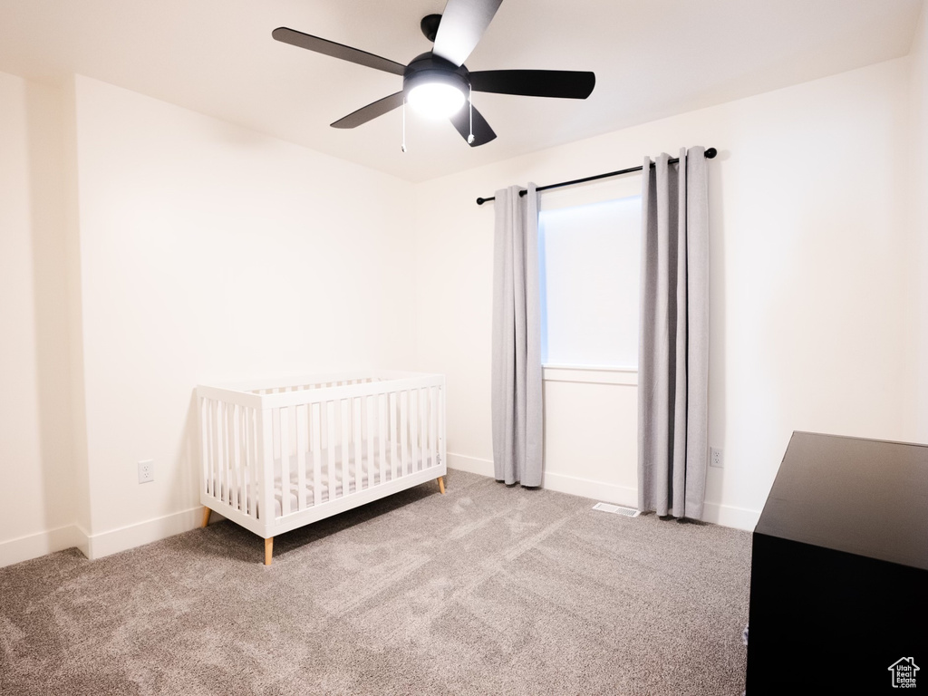 Carpeted bedroom with a ceiling fan, baseboards, and a crib