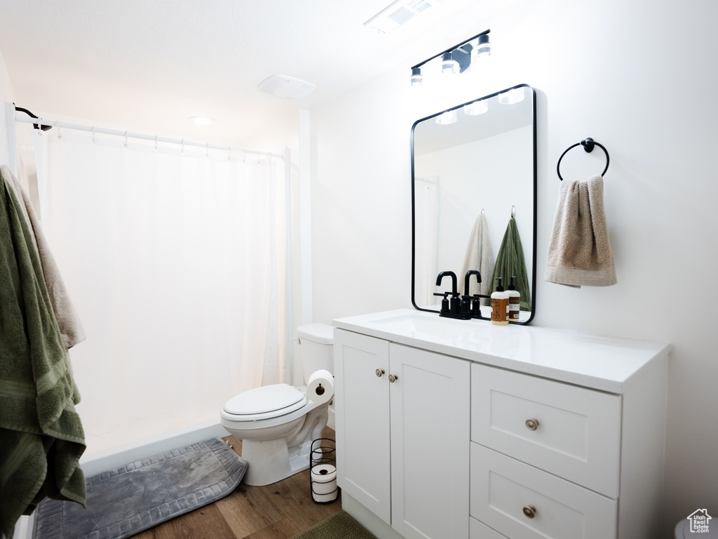 Bathroom featuring a shower with curtain, visible vents, wood finished floors, vanity, and toilet