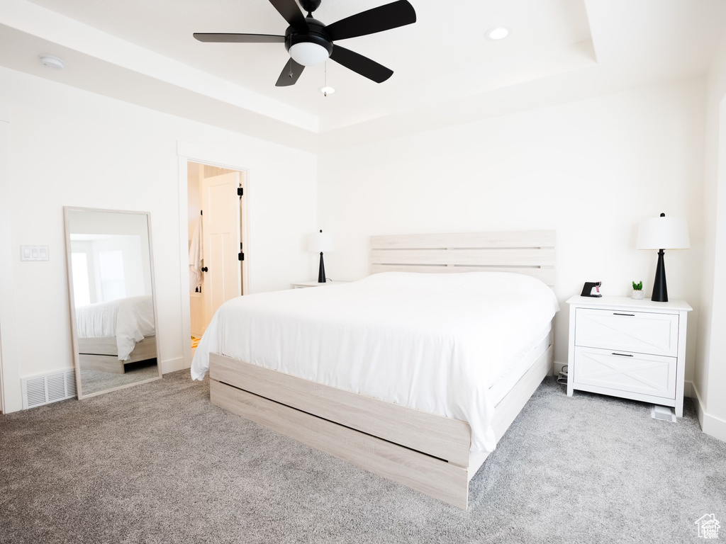 Bedroom with a raised ceiling, a ceiling fan, carpet flooring, and visible vents