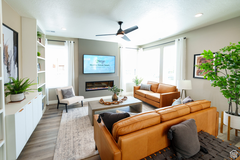 Living area with a fireplace, light wood-type flooring, a ceiling fan, and recessed lighting