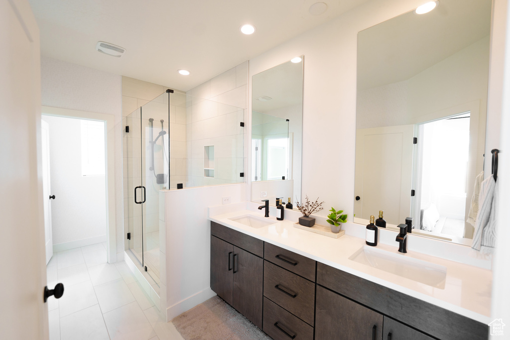 Ensuite bathroom with tile patterned floors, a shower stall, double vanity, and a sink