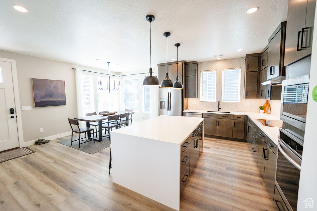 Kitchen featuring a sink, stainless steel appliances, light countertops, a kitchen island, and backsplash