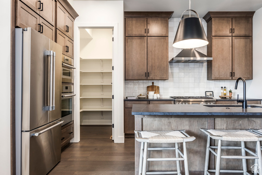Kitchen featuring dark countertops, appliances with stainless steel finishes, tasteful backsplash, dark wood finished floors, and a sink