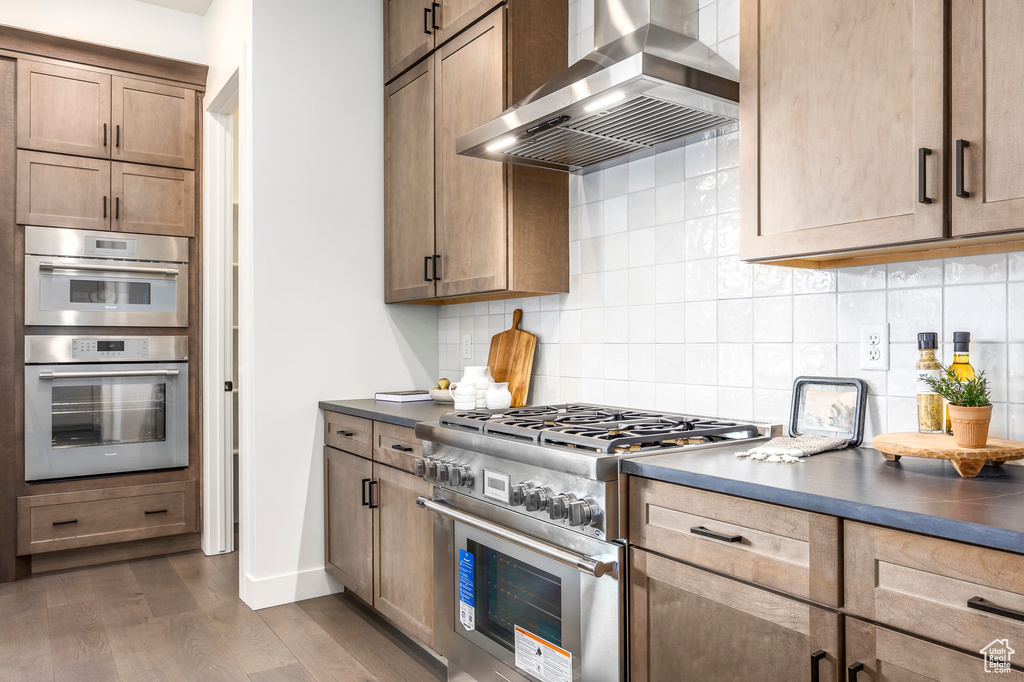 Kitchen featuring dark wood-style flooring, stainless steel appliances, dark countertops, and wall chimney exhaust hood