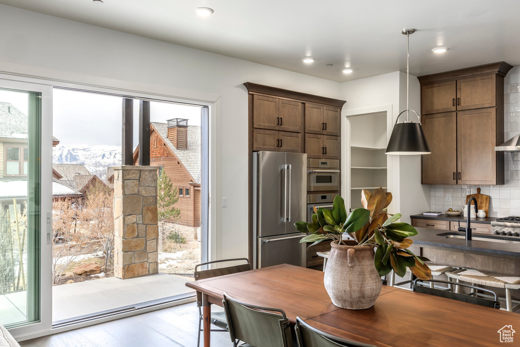 Kitchen with wood finished floors, dark countertops, high end fridge, a sink, and backsplash