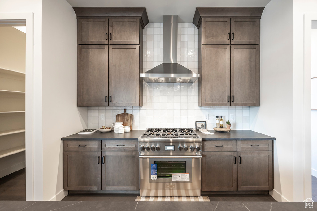 Kitchen featuring dark countertops, backsplash, high end stainless steel range oven, and wall chimney range hood