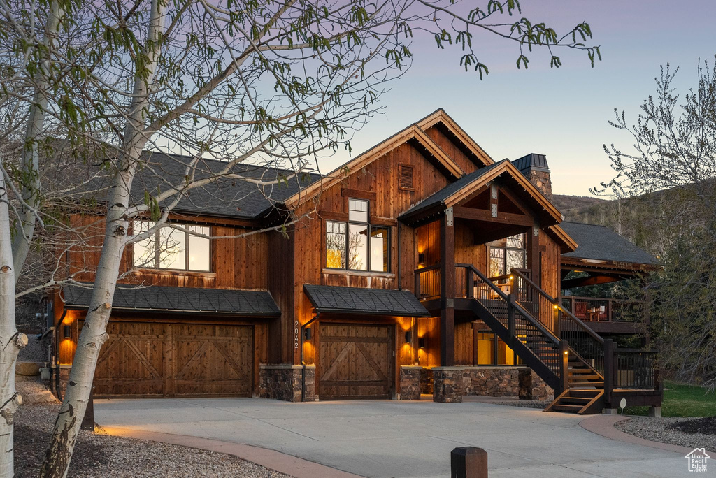 Rustic home featuring stone siding, a garage, stairway, a chimney, and concrete driveway