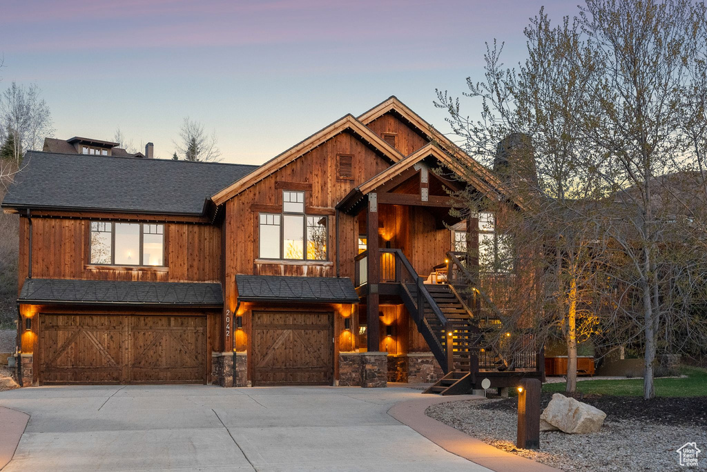 View of front of property with stone siding, a chimney, concrete driveway, an attached garage, and stairway