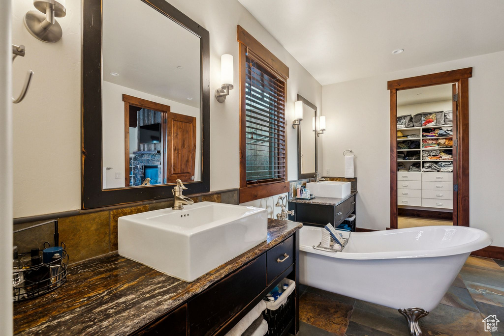 Full bath with stone finish flooring, a freestanding bath, two vanities, and a sink