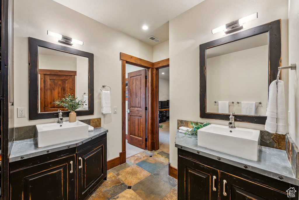 Full bath featuring stone finish flooring, visible vents, two vanities, and a sink