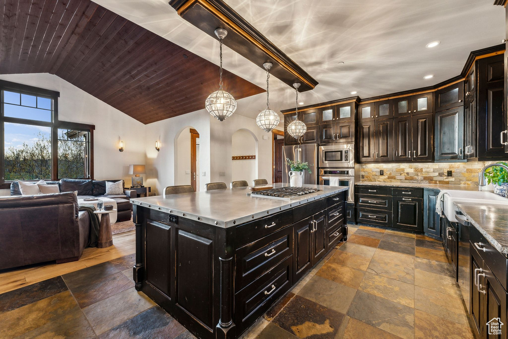 Kitchen featuring stone tile flooring, a sink, open floor plan, arched walkways, and stainless steel appliances