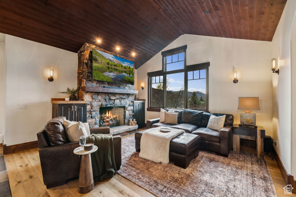 Living room featuring high vaulted ceiling, wood-type flooring, wood ceiling, and a stone fireplace