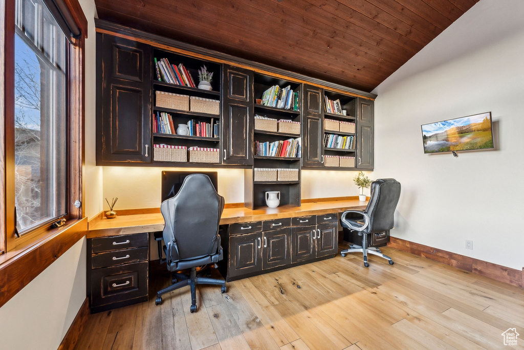 Office area featuring baseboards, vaulted ceiling, built in study area, and light wood-style floors