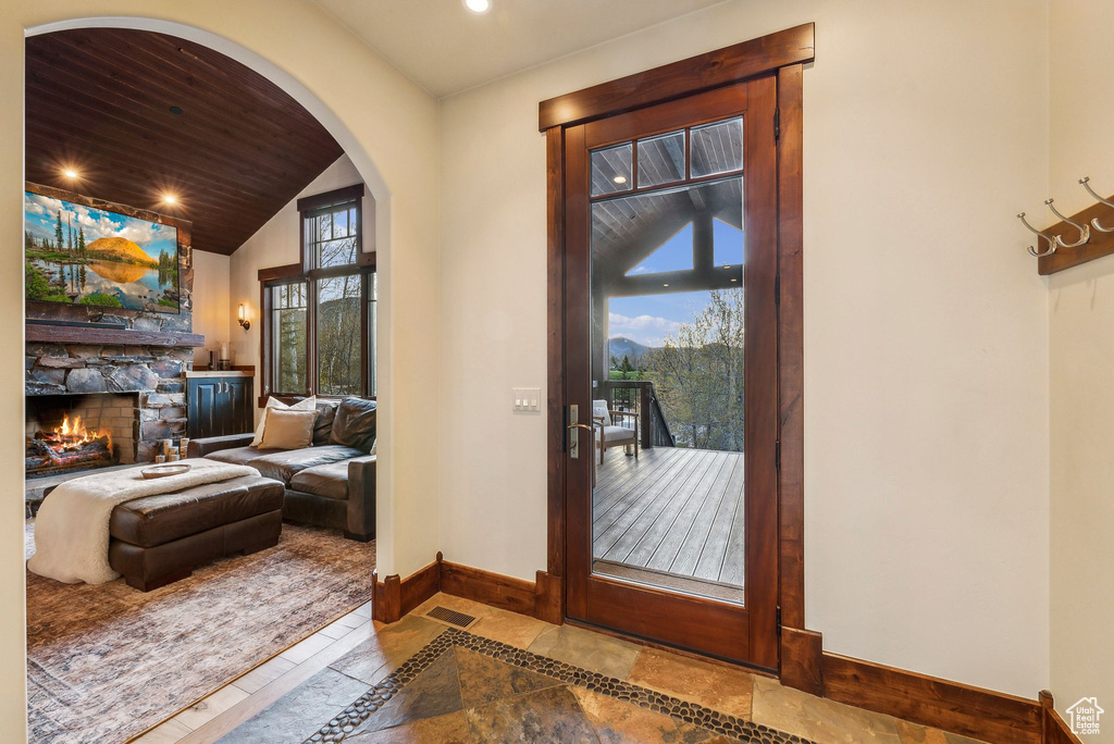 Entryway with baseboards, vaulted ceiling, a stone fireplace, and a healthy amount of sunlight