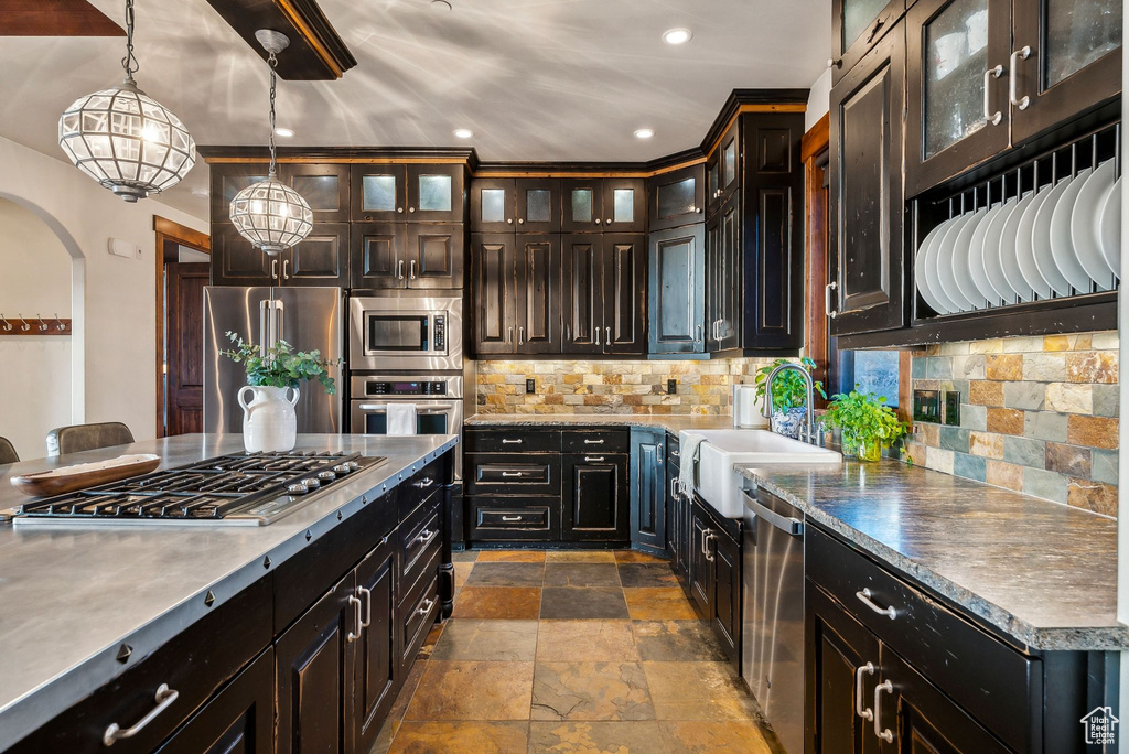 Kitchen featuring decorative backsplash, appliances with stainless steel finishes, arched walkways, a sink, and stone tile flooring