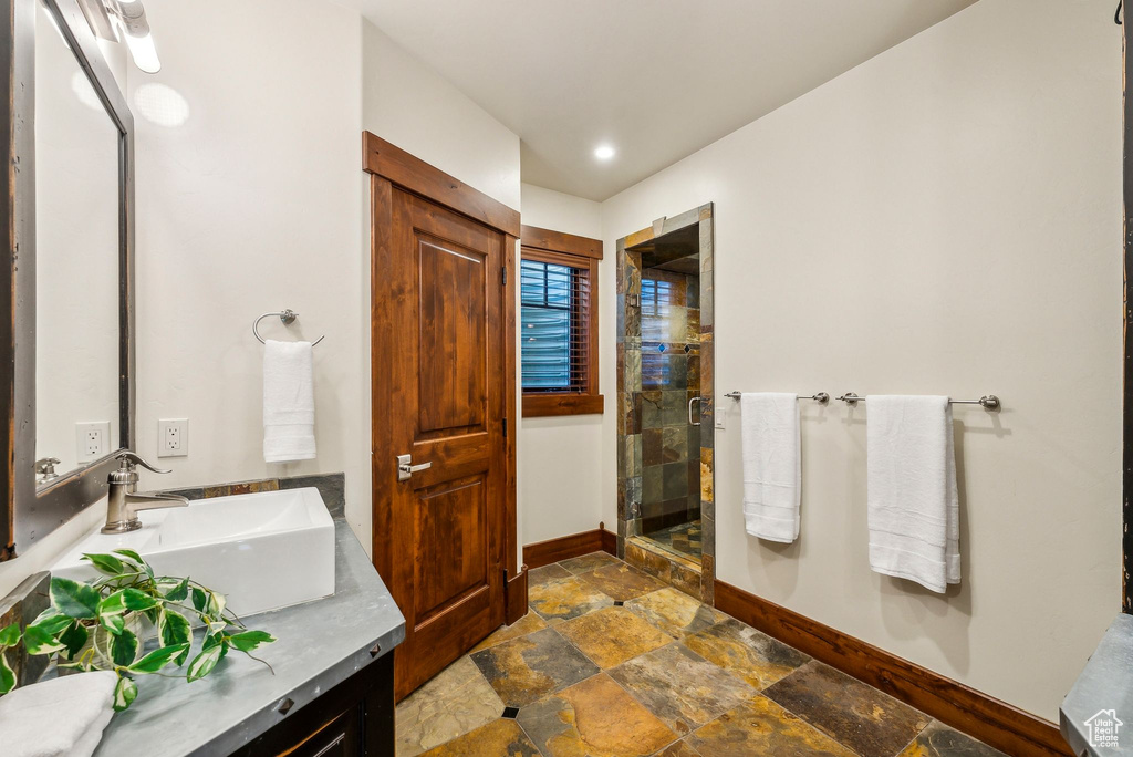 Bathroom featuring vanity, baseboards, stone finish floor, and a shower stall