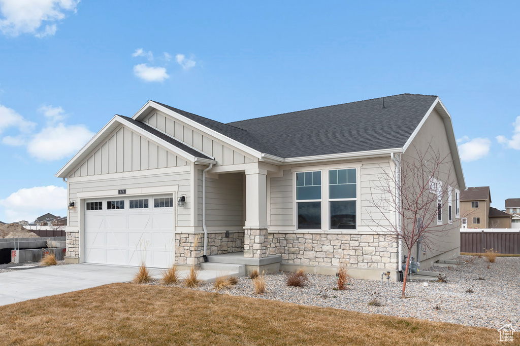 Craftsman-style house featuring board and batten siding, driveway, fence, an attached garage, and stone siding