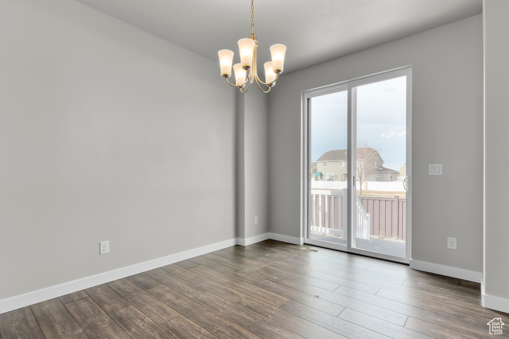 Empty room with baseboards, a chandelier, and dark wood-type flooring