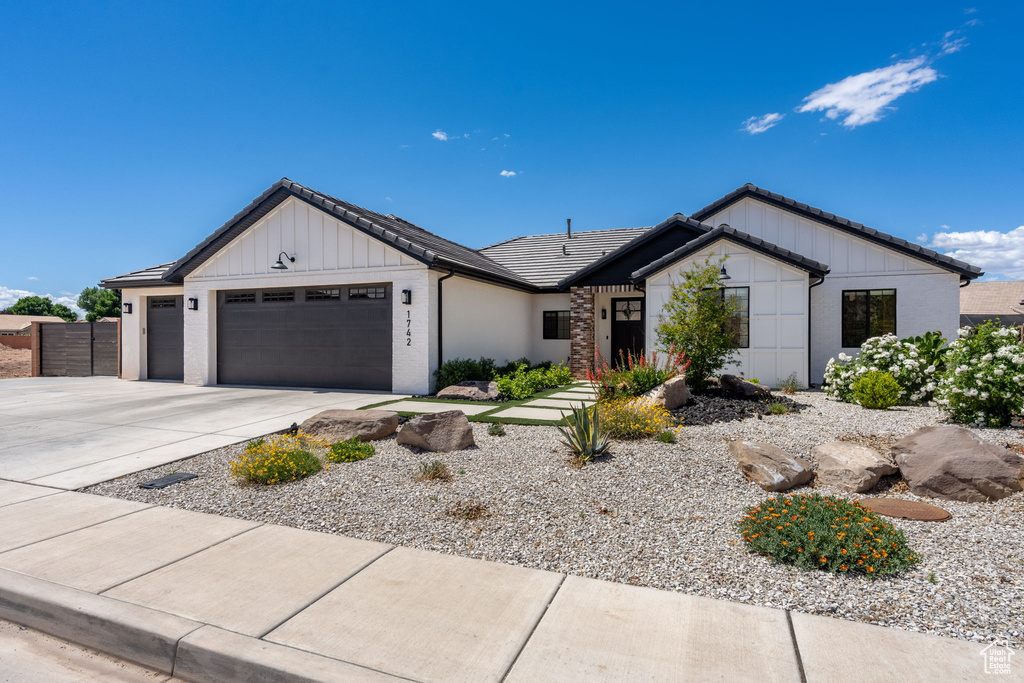 View of front of house with board and batten siding, a tile roof, a garage, fence, and concrete driveway
