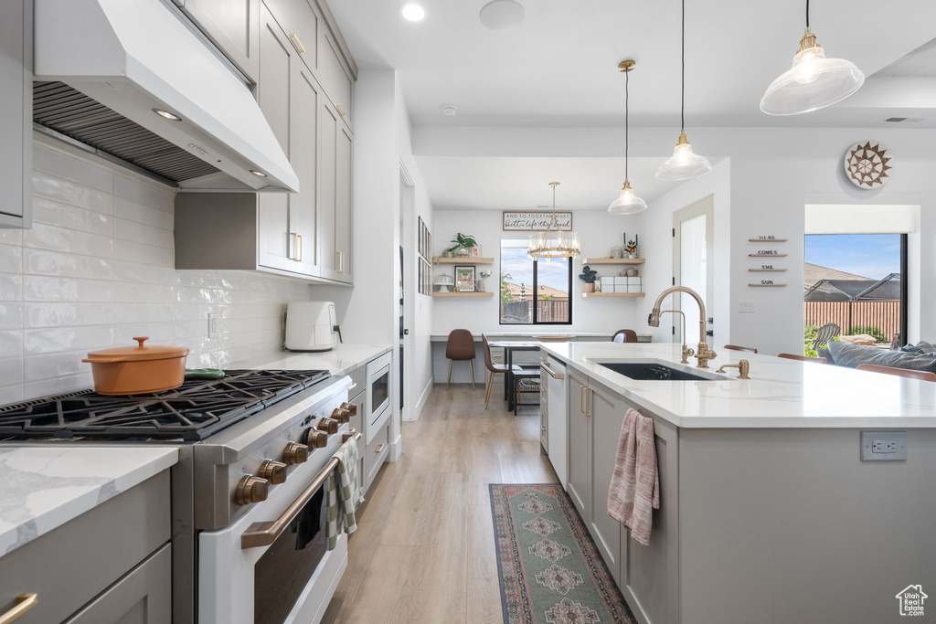 Kitchen with a sink, white appliances, a healthy amount of sunlight, under cabinet range hood, and gray cabinetry