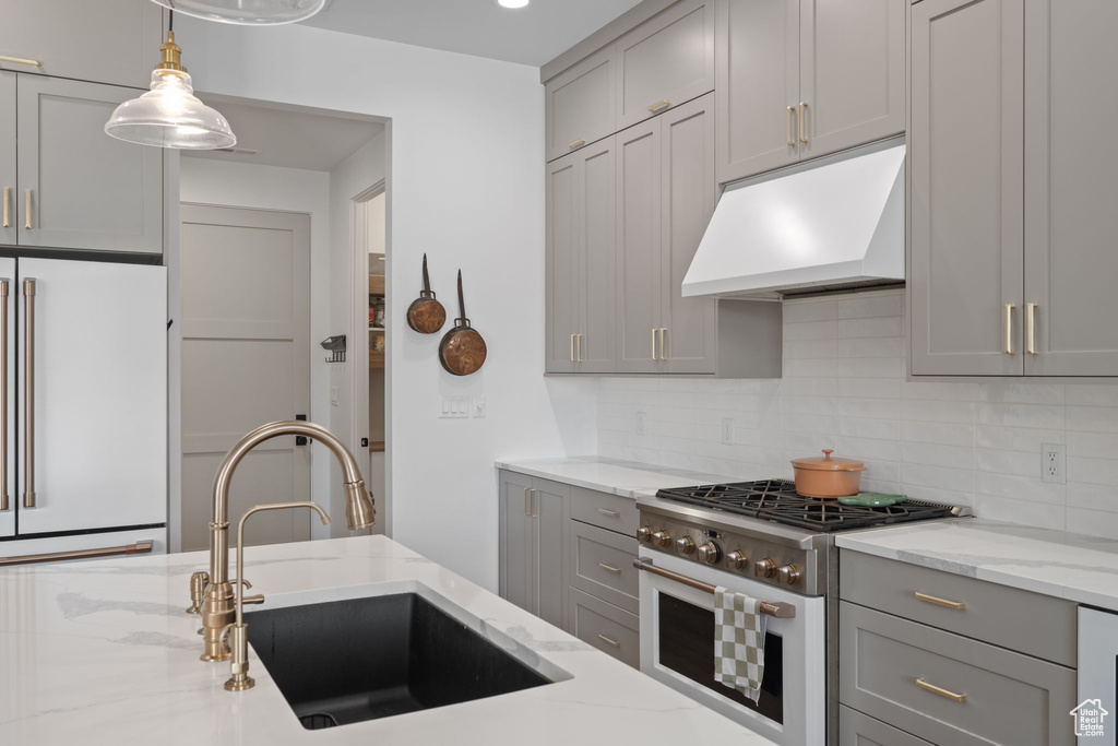 Kitchen featuring gray cabinets, backsplash, high quality appliances, a sink, and under cabinet range hood