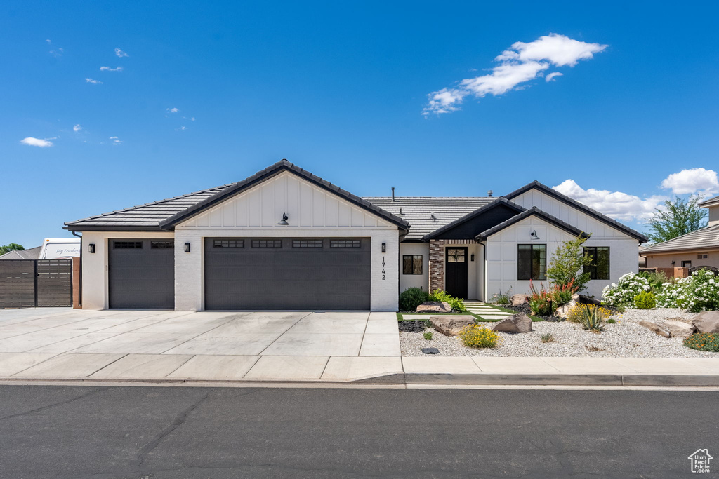 Ranch-style house featuring a garage, board and batten siding, driveway, and a tile roof