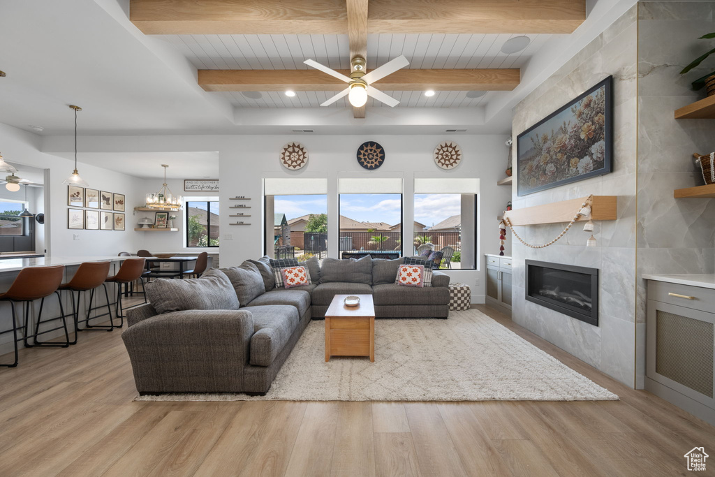 Living room with a fireplace, a ceiling fan, beam ceiling, and light wood-style floors