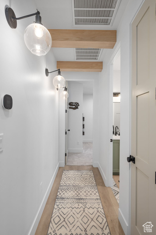 Hallway with a sink, baseboards, light wood-type flooring, and visible vents