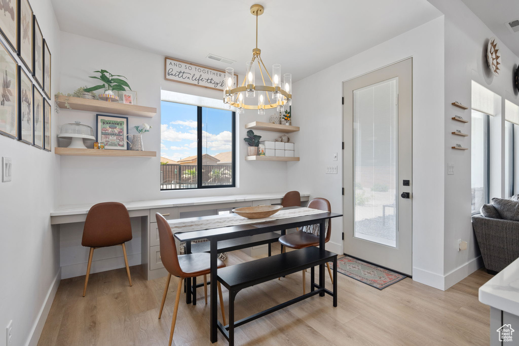 Dining space with an inviting chandelier, built in desk, visible vents, and light wood-type flooring