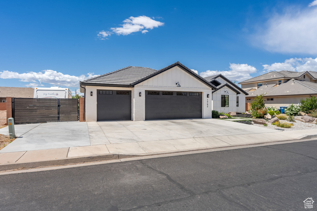 View of front facade featuring an attached garage, board and batten siding, a gate, concrete driveway, and a tiled roof